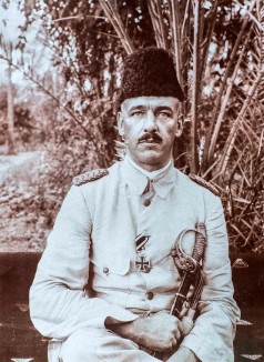 Fritz Klein in weißer Uniform mit Säbel und orientalischer Kopfbedeckung sitzend vor einem Busch