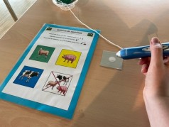 digitale Tafel auf Tisch mit verschiedenen Tieren, rechts eine Hand mit Stift