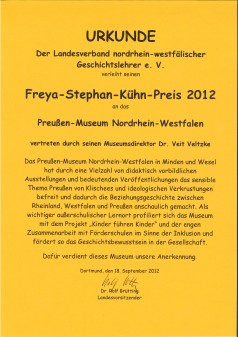 Auf dem Bild ist eine Urkunde auf gelbem Hintergrund mit der Überschrift Freya-Stephan-Kühn Preis 2012 an das Preußen-Museum Nordrhein-Westfalen mit weiterem Text zu sehen.