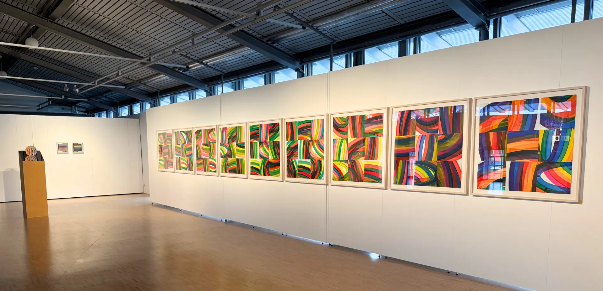 Das Bild zeigt bunte Bilder, die an einer Wand hängen. 