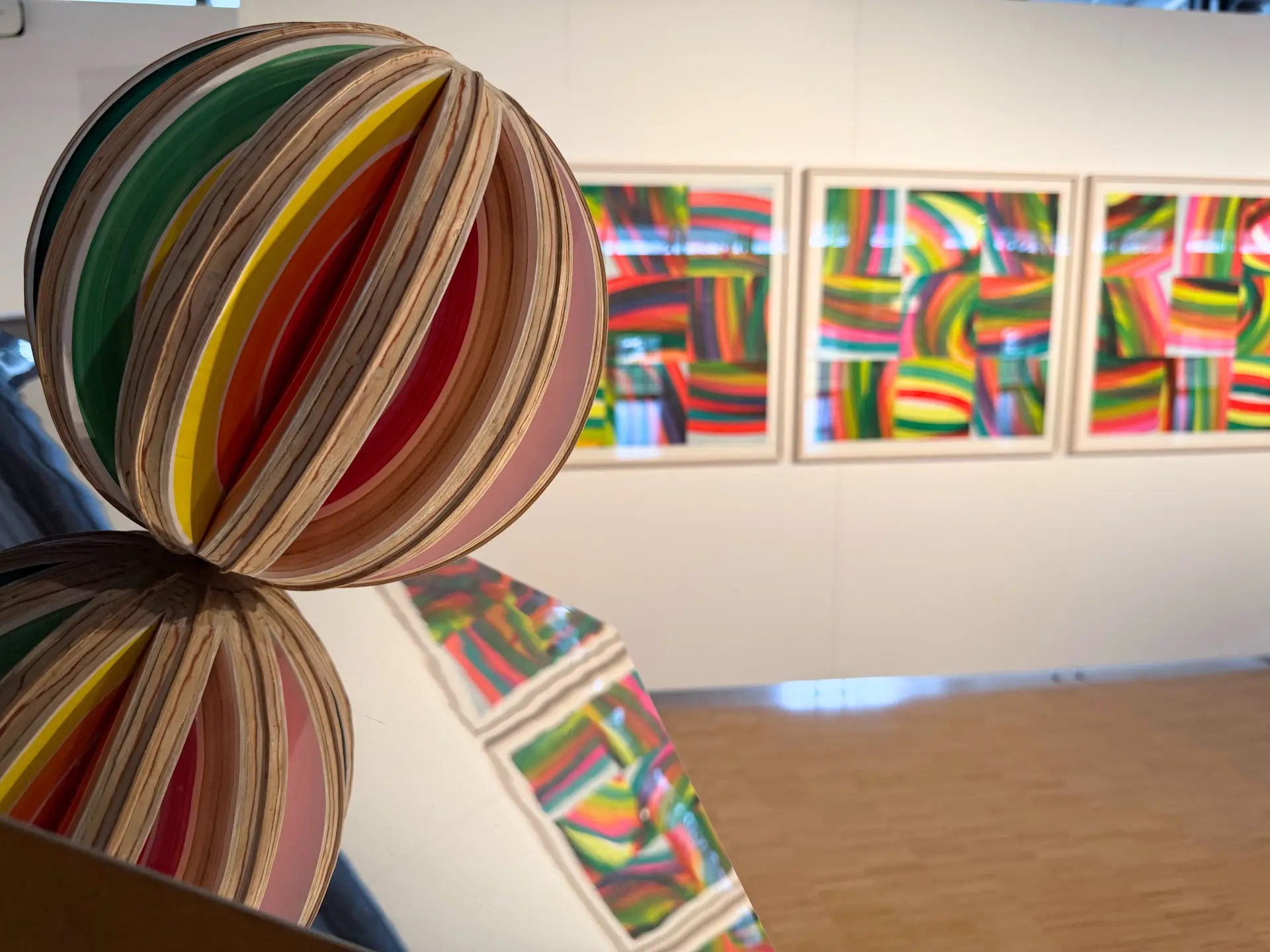 Das Bild zeigt im Vordergrund eine bunte Kugel, dahinter bunte Bilder an einer Wand. 