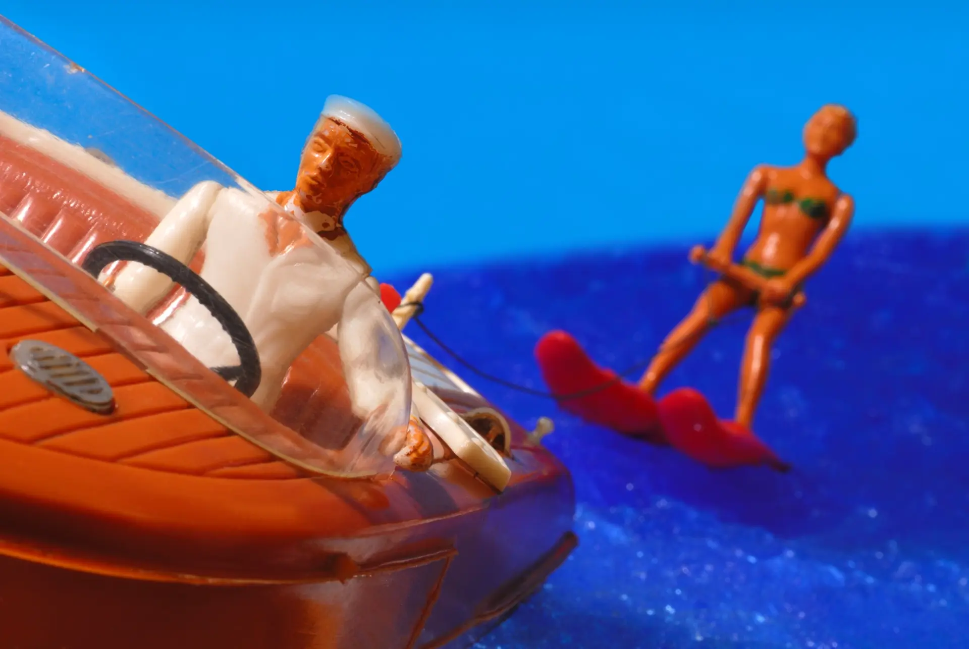 Ein Plastikspielzeugboot mit einer Spielzeugfigur am Steuer zieht eine Spielzeugfigur auf Wasserski