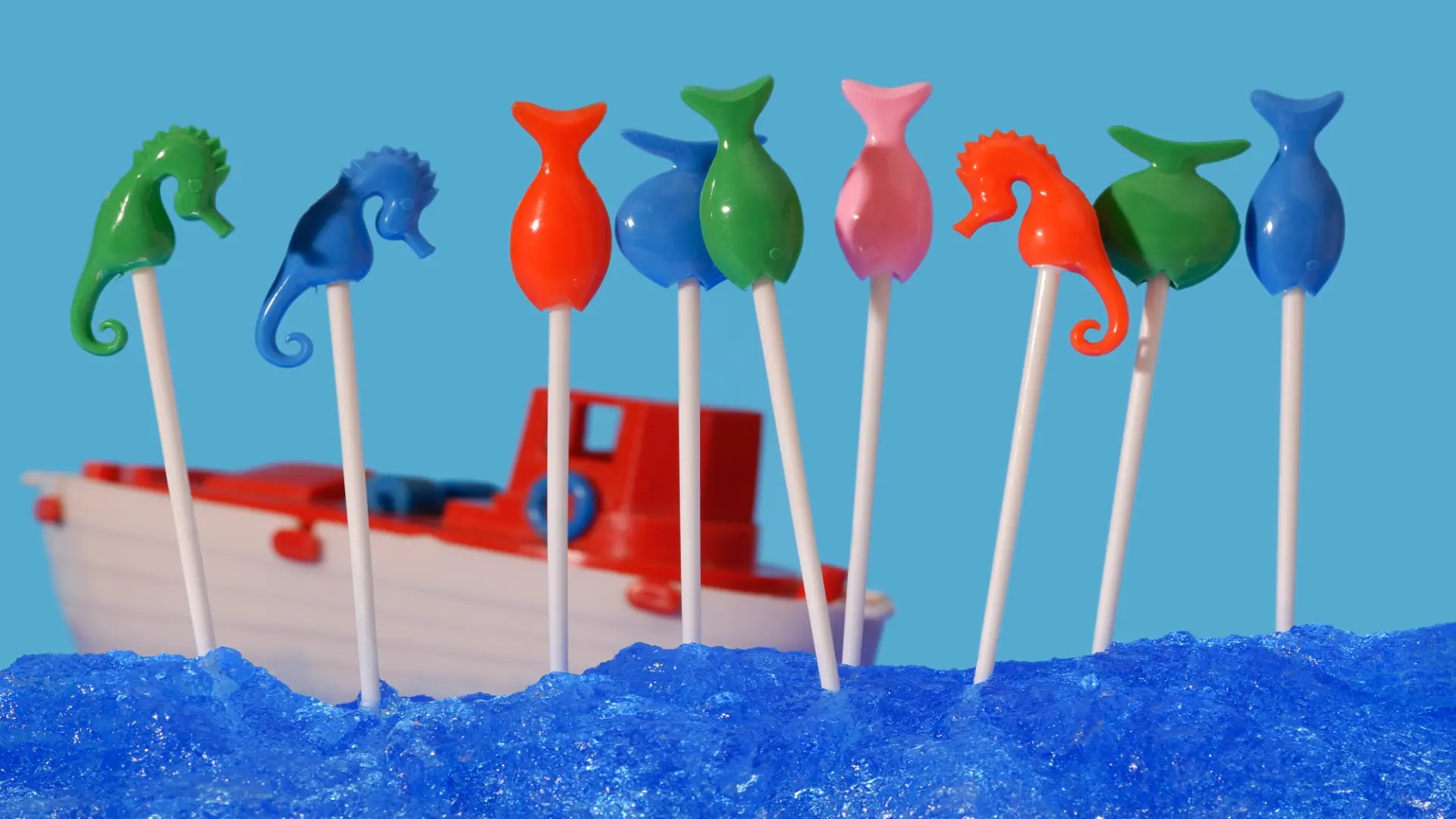 Ein Plastikspielzeugboot fährt auf einem imitierten Meer. Im Vordergrund stehen Plastikseepferdchen auf Stöckchen