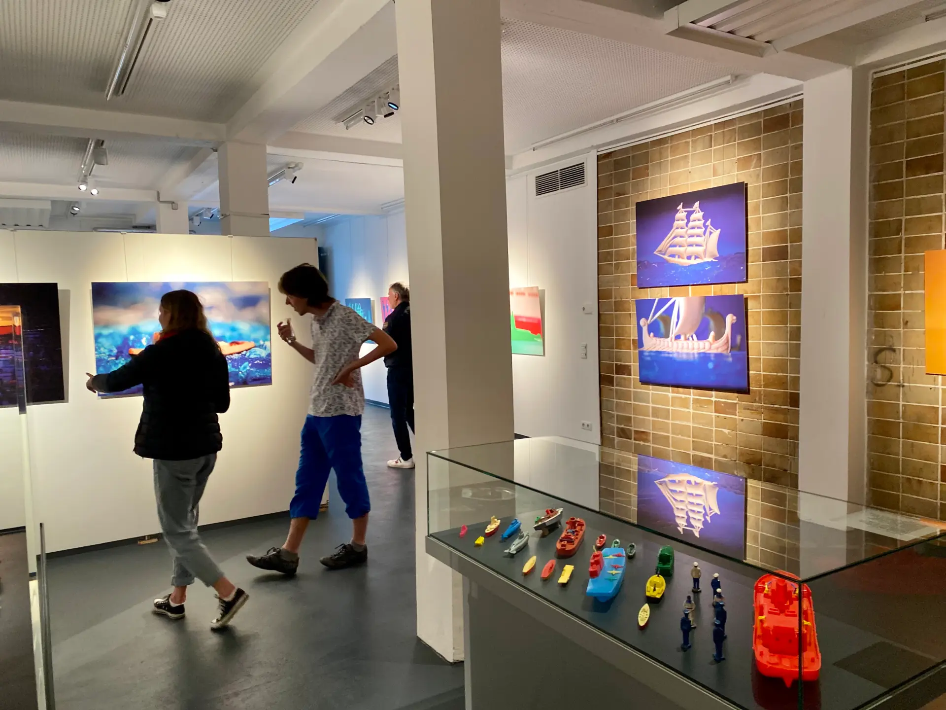 Die Ausstellung Leinen los zeigt verschiedene Fotos mit Spielzeugschiffen aus Plastik in einem Ausstellungsraum 